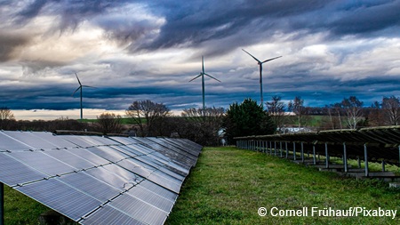 Teile einer Freiflächensolaranlage auf einer Wiese, im Hintergrund Windenergieanlagen