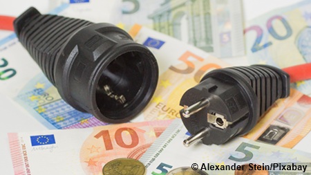 Stromstecker auf Geldscheinen und Münzen liegend